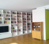 Foto:   Regalwand und Stauraumcubus mit grünen Schiebetüren in offenen großen Raum.